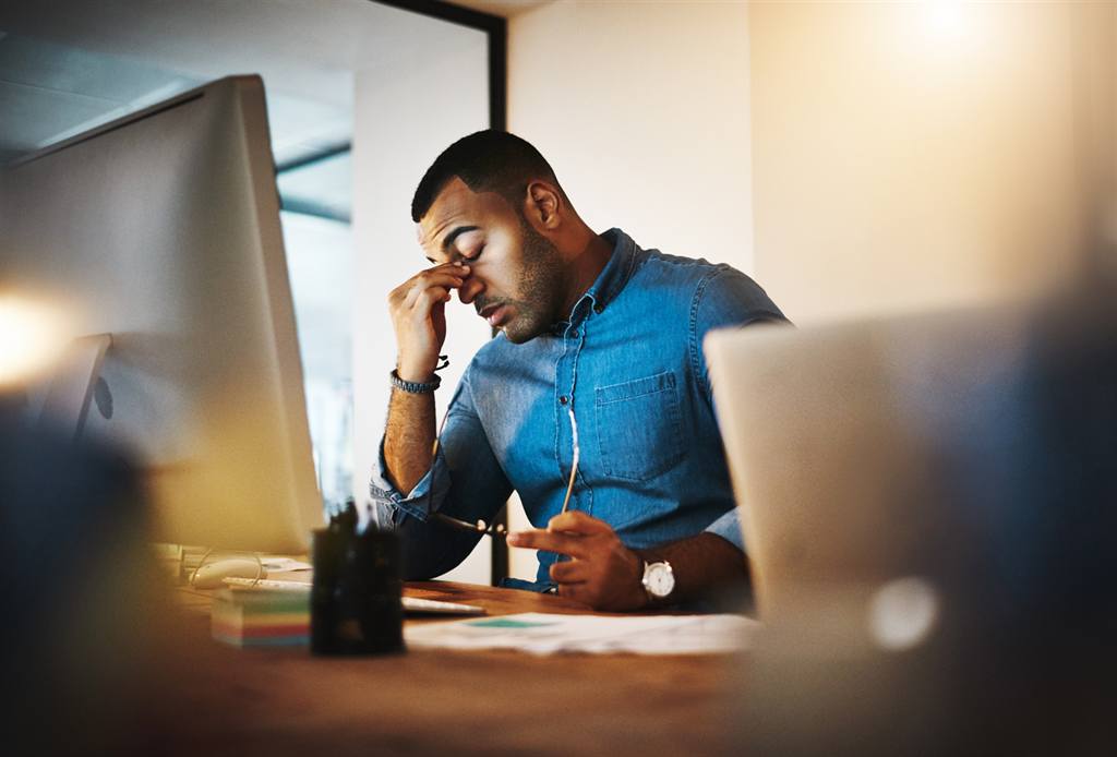 Homem cansado em frente ao computador com sinais de esgotamento